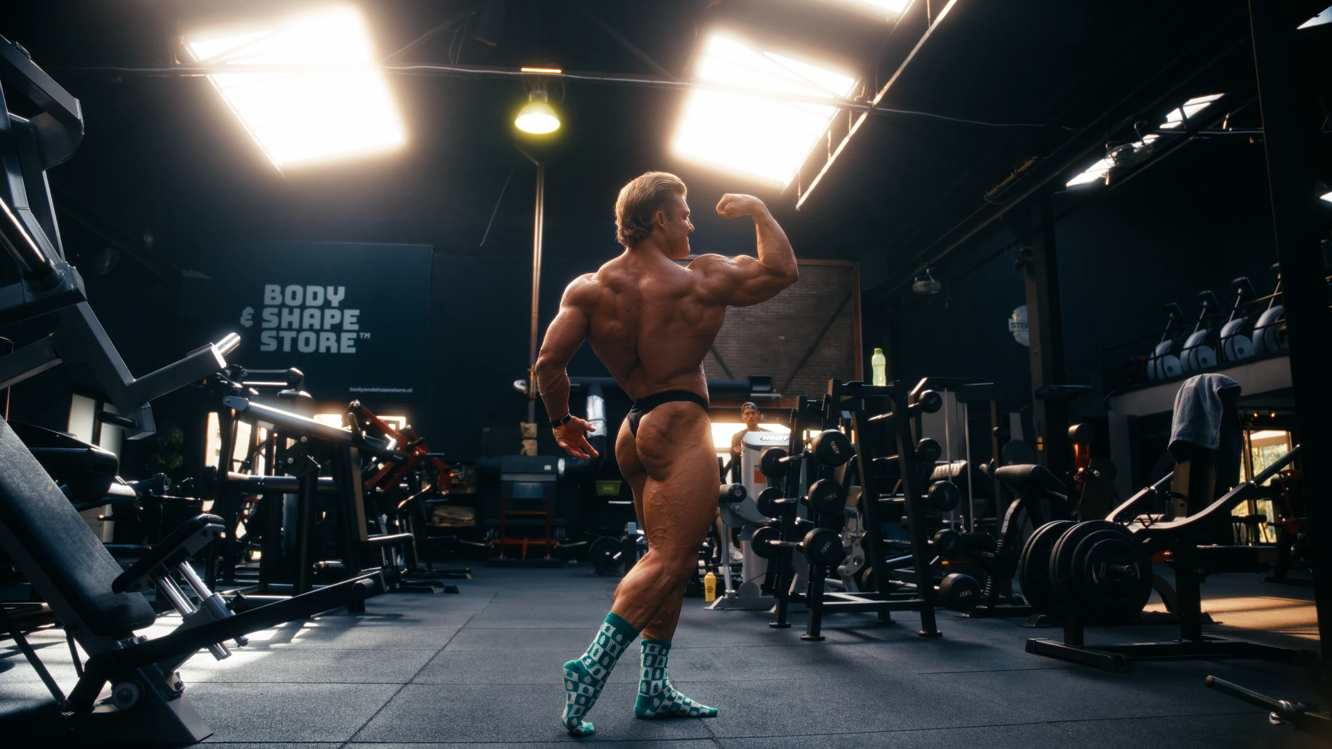 Bodybuilder poseert van opzij in de gym, met één arm gebogen