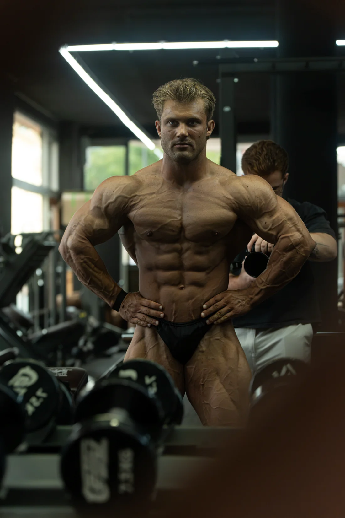 Bodybuilder poseert voor de spiegel en een rij dumbbells